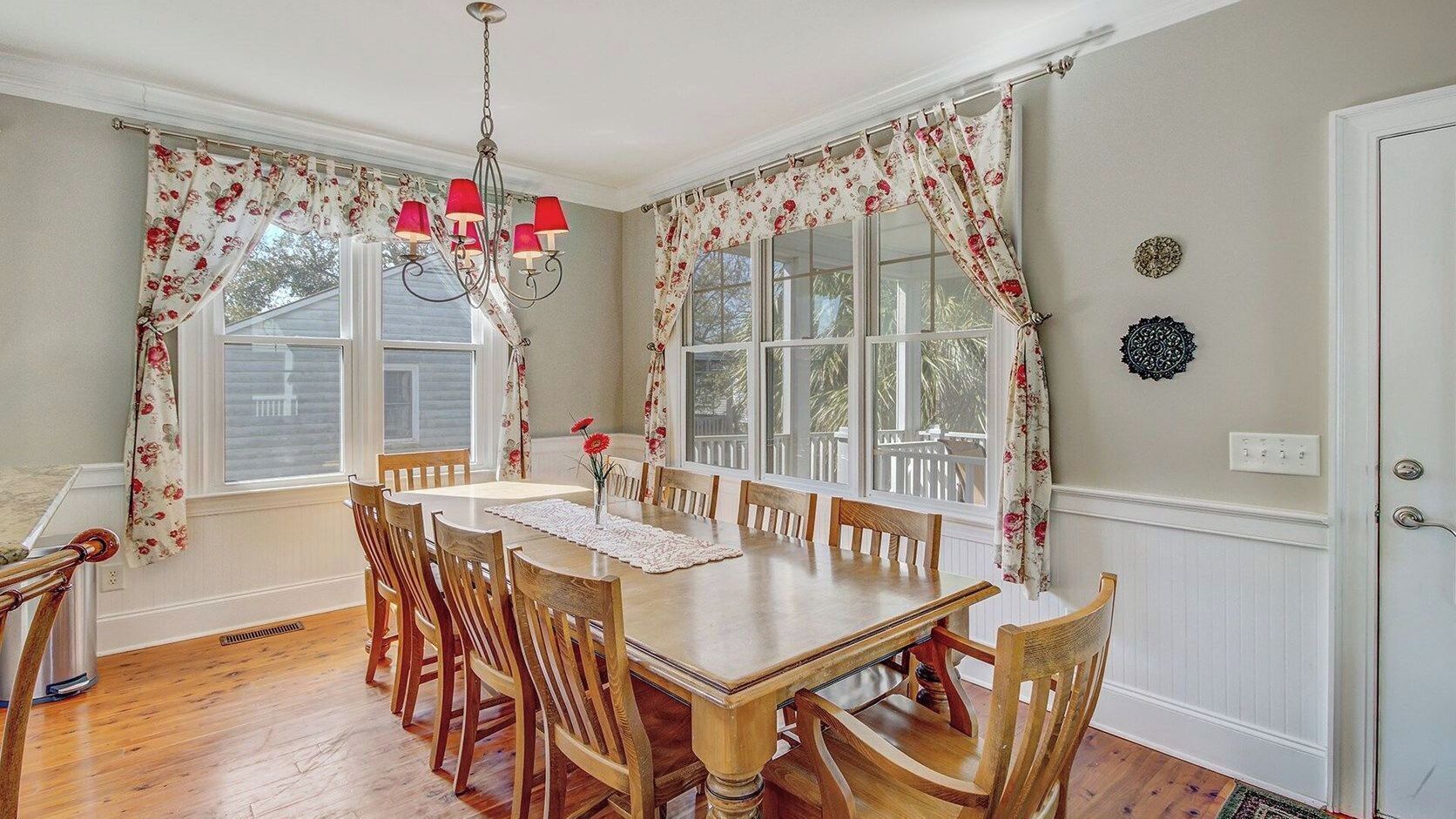 A dining room with a wooden table, chairs, floral curtains, and a chandelier.