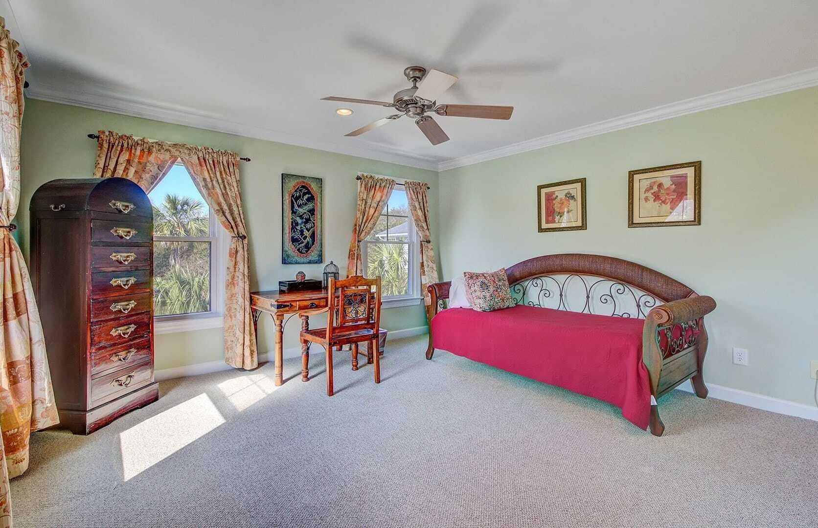 Une chambre à coucher comprenant un lit, un bureau, une chaise, une commode et un ventilateur de plafond.