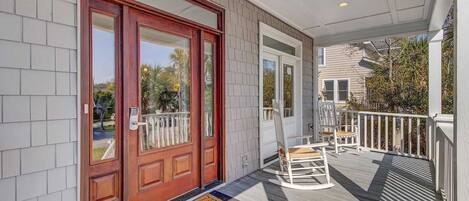 A porch with a wooden door, a white chair, and a small table.