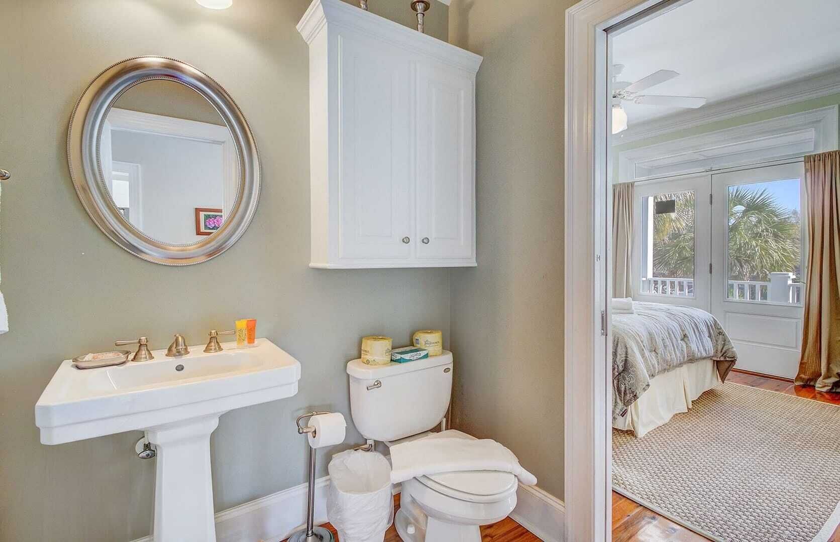 Un baño con lavabo, inodoro y espejo, y un dormitorio con cama y ventana.