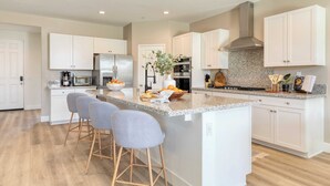 A modern kitchen with white cabinetry, a granite countertop, and a central island with bar stools. - Sleeps 16! Pool Oasis w/ Game Room, Hot Tub, Fire Pit Desert Eden by Avantstay (Coachella)