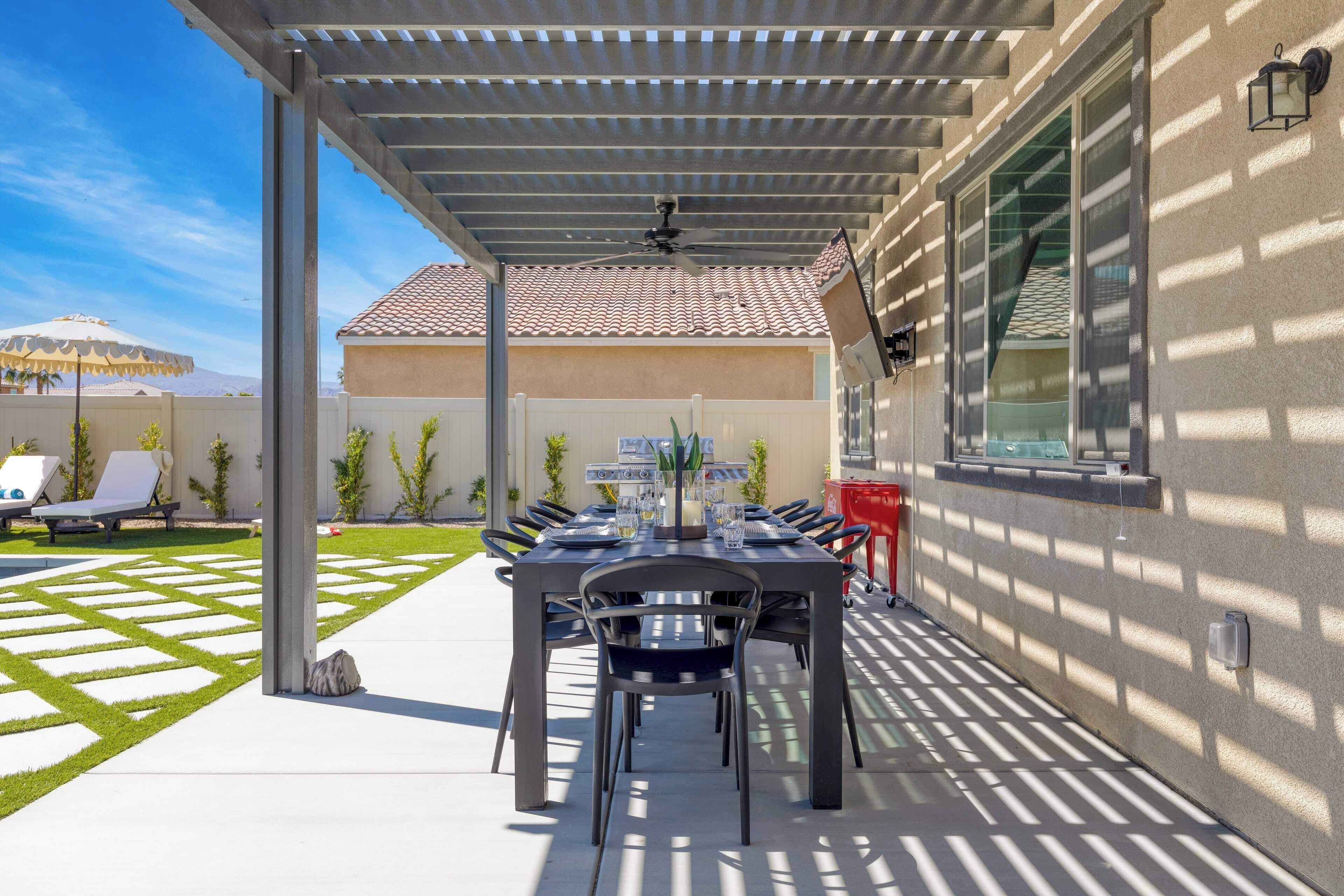 Un patio exterior con mesa y sillas de comedor cubiertas, y un ventilador de techo.