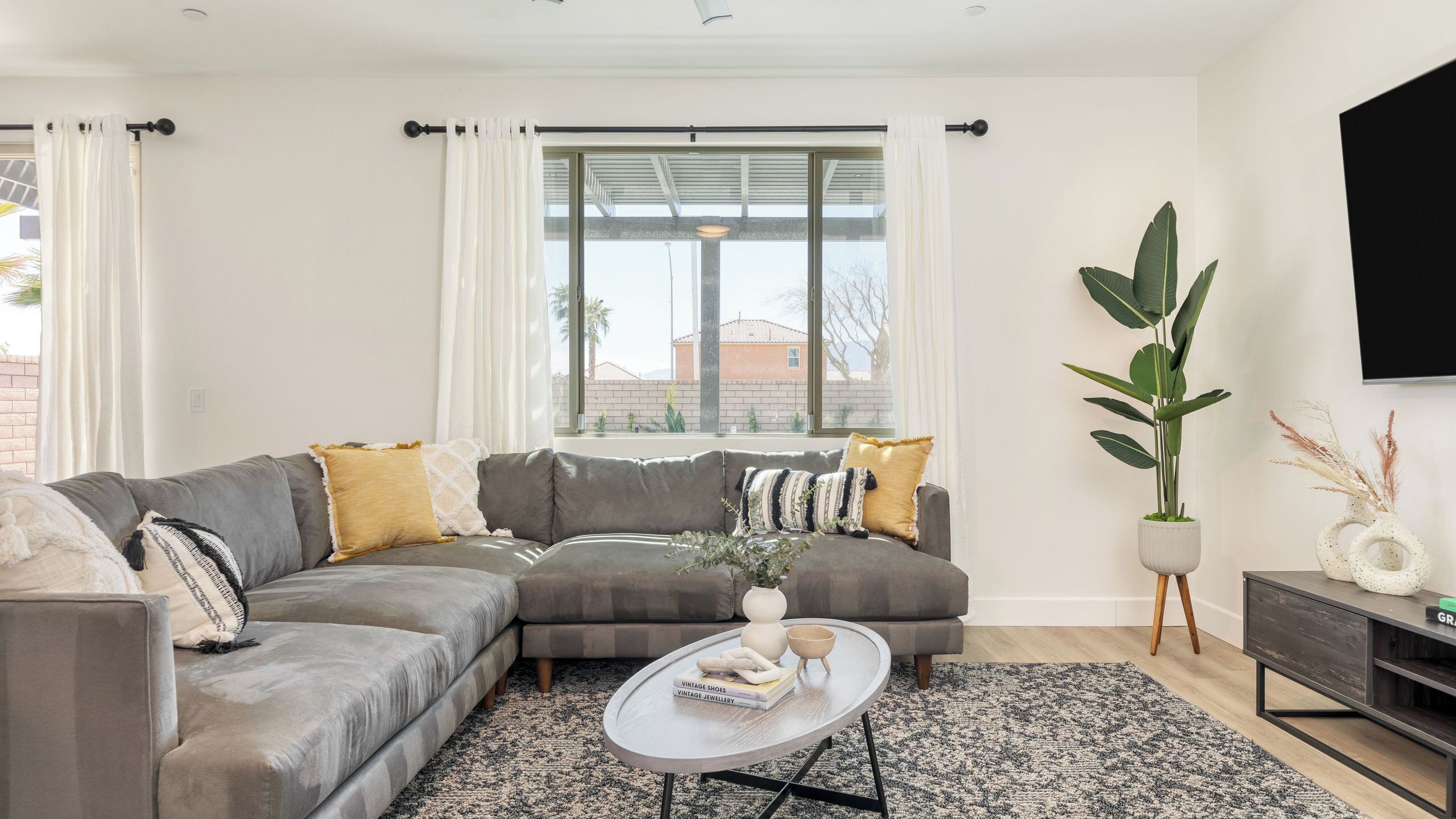 A modern living room with a sectional sofa, a coffee table, and a large window with curtains.