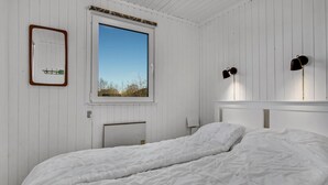 Un dormitorio con cama, ventana, espejo y lámpara de pared.