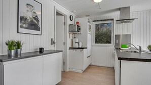 Una cocina compacta con armarios blancos, un microondas, una cafetera y una ventana con vistas a árboles.