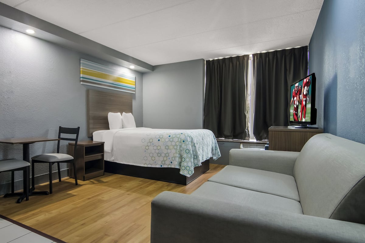 Une chambre d’hôtel comprenant un lit, un canapé, un bureau avec des chaises, une télévision et une fenêtre avec des rideaux.