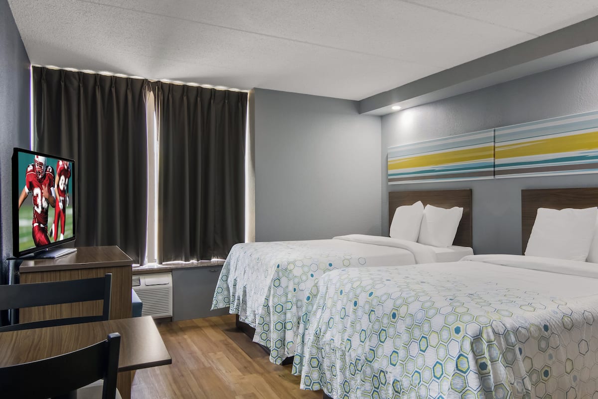 Une chambre d’hôtel avec deux lits, une télévision, un bureau et une fenêtre avec des rideaux.