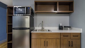 Une cuisine compacte équipée d’un réfrigérateur en acier inoxydable, d’un four à micro-ondes, d’un évier et de meubles de rangement en bois.