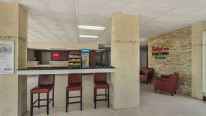 Un espace d’accueil avec un comptoir, trois tabourets de bar, un distributeur automatique et une enseigne « Red Roof Home Town Studios ».