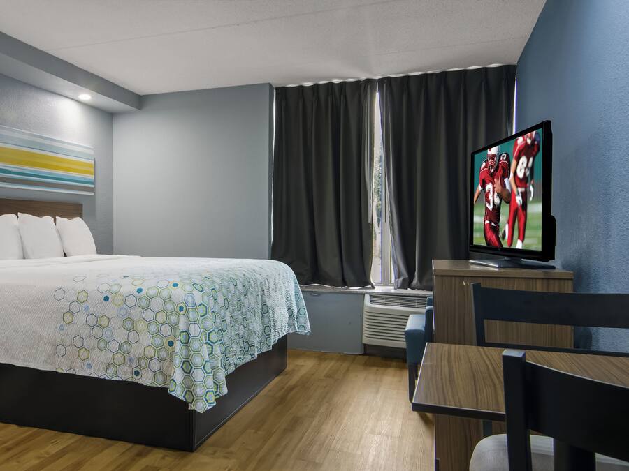 Quarto de hotel com cama, televisão, secretária e uma cadeira.