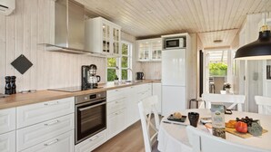Una cocina moderna con armarios blancos, horno empotrado, cafetera y comedor con mesa lista para el desayuno.