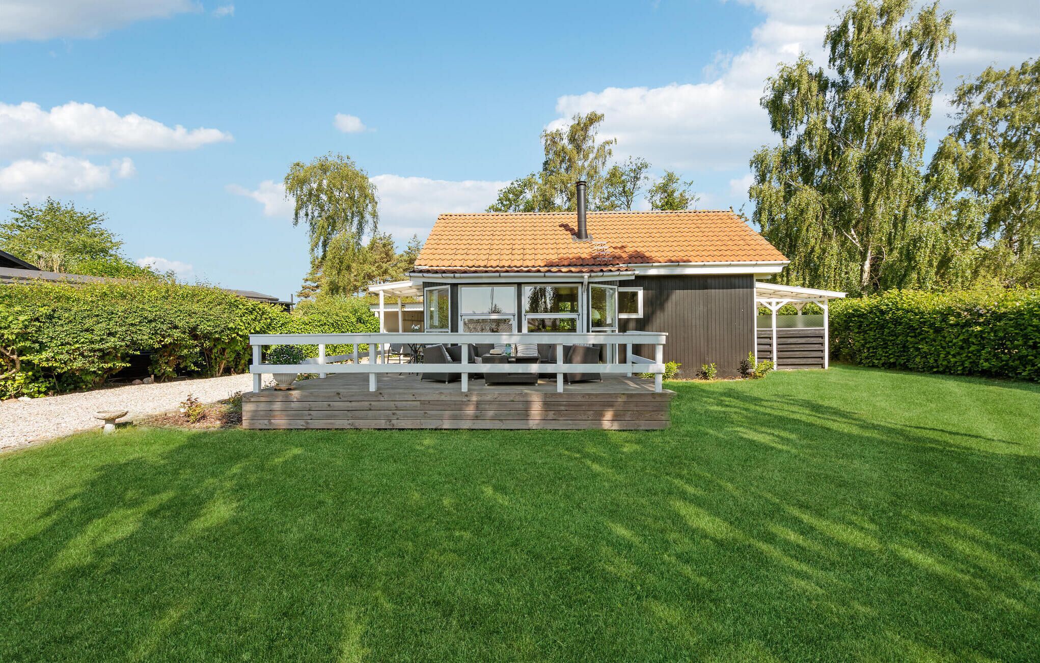 A modern house with a covered patio, a fenced deck, and a well-maintained lawn.