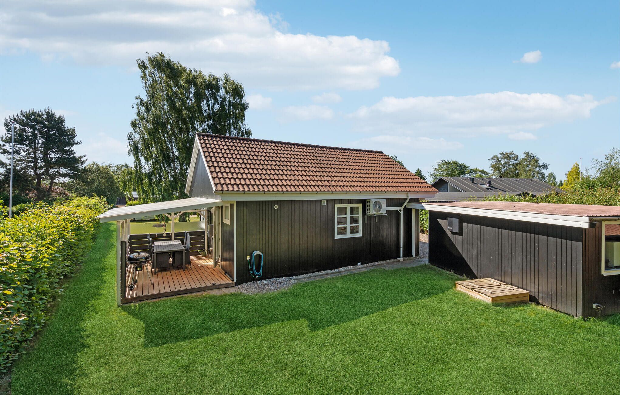 Ein zweistöckiges Haus mit einem Ziegeldach, einer überdachten Terrasse mit Gartenmöbeln und einem gepflegten Rasen.