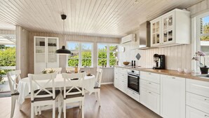 Una cocina moderna con armarios blancos, una isla central y un comedor con sillas blancas.
