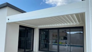 Una casa moderna con patio coperto, ampie porte scorrevoli in vetro e una zona relax esterna ben visibile.