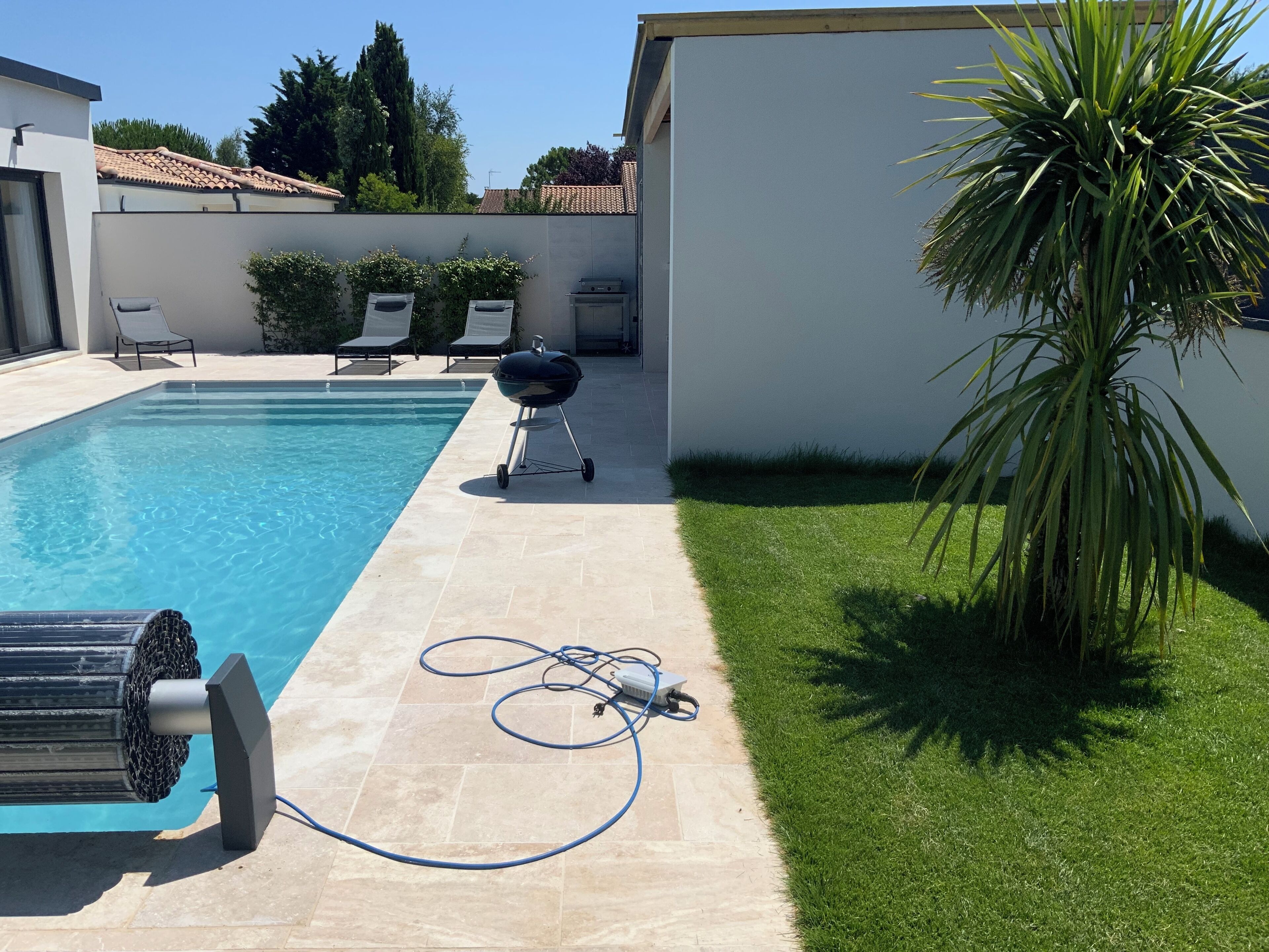 A swimming pool with a tiled deck, a grill, and a hose.