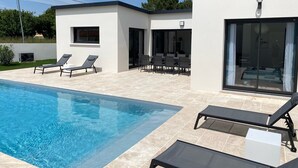 Area piscina moderna all'aperto con poltrone relax e zona pranzo.