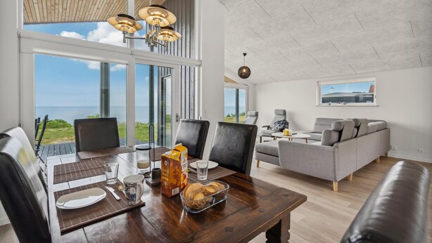A modern living room with a large window overlooking a scenic view, a dining area with a wooden table, and a cozy seating area with a sofa and armchairs.