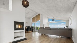 A modern living room with a fireplace, a large gray sofa, and a dining area with chairs.