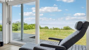A modern room with a large sliding glass door leading to a deck with a view of a grassy area and a body of water.
