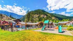 A playground with slides and a pool area, surrounded by houses and mountains. - Icicle Village Blizzard Pool Parking (Leavenworth)