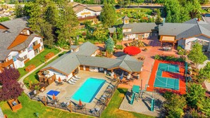 An aerial view of a residential area with a swimming pool, tennis court, and houses with distinct architectural styles. - Icicle Village Blizzard Pool Parking (Leavenworth)