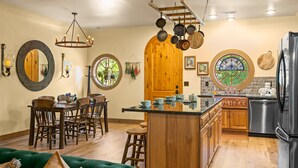 A kitchen with a wooden island, a dining area with a green sofa, and a large wooden door. - Howards Hollow! Earth Home at The Forgotten Forest! (Kodak)