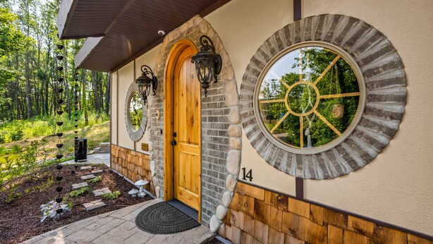 A house with a wooden door, stone walls, and a circular window with a decorative frame. - Howards Hollow! Earth Home at The Forgotten Forest! (Kodak)