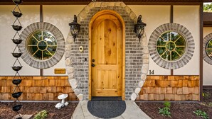 A wooden door with a stone archway, two lantern-style lights, and a circular window on each side. - Howards Hollow! Earth Home at The Forgotten Forest! (Kodak)