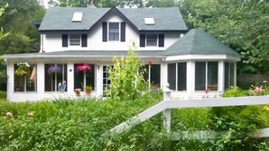 A two-story house with a covered porch and a small gazebo.