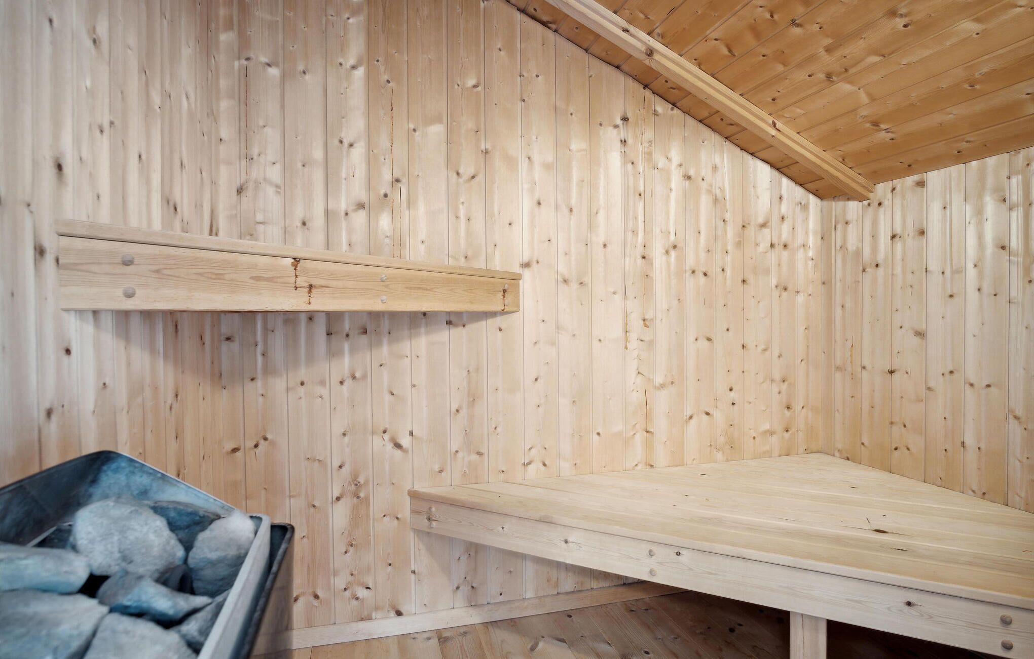 Interior de uma cabana de madeira com beliche, prateleira pequena e lixeira.