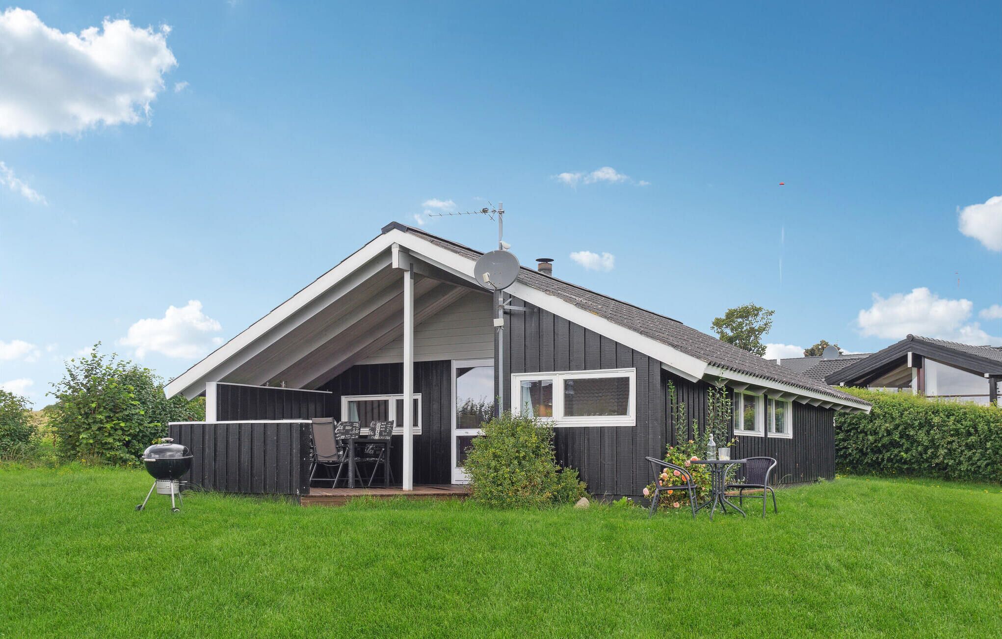 Ein modernes Haus mit geneigtem Dach, einer Satellitenschüssel und einem Grill im Garten.