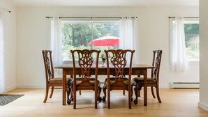 A dining area with a wooden table and chairs, large windows with curtains, and a red umbrella outside. - Ski - Luxury Retreat Home - Stream, Waterfalls! (Palenville)