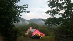 A pink house with a car parked in front, surrounded by greenery and a stone wall. - Ski - Luxury Retreat Home - Stream, Waterfalls! (Palenville)