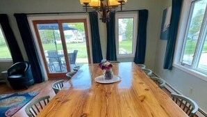 Una sala da pranzo con un tavolo di legno, sedie, un lampadario e vista sull'esterno attraverso ampie finestre.