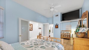 Quarto com cama, ventilador de teto, televisão e cómoda de madeira.