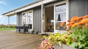 Et moderne hus med træterrasse, store vinduer og udendørs møbler.