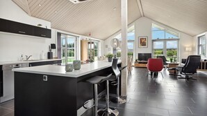 Et moderne køkken med en stor ø, sorte barstole og et spiseområde med en rød stol.