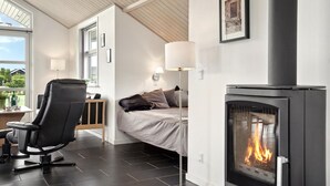 Et moderne soveværelse med pejs, seng, skrivebord med stol og et vindue med udsigt til grønne områder.