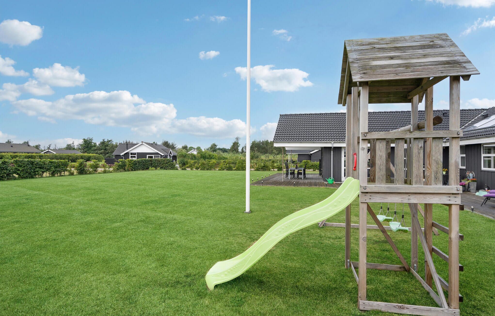 Une structure de jeu en bois avec un toboggan, installée dans une cour gazonnée.