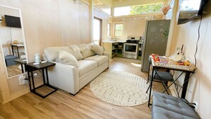 Ein kompakter Wohnbereich mit einer Couch, einem kleinen Tisch, einem runden Teppich und einer Küchenzeile im Hintergrund.