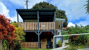 A two-story building with a balcony, a staircase leading to the entrance, and a garden area with plants and a small table.