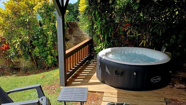 A covered outdoor area with a hot tub, wooden deck, and seating.