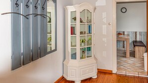A hallway with a white cabinet with glass doors, a wall-mounted coat rack, and a door leading to a kitchen area.