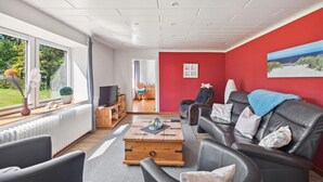 A modern living room with a red accent wall, a leather sofa, a wooden coffee table, and a television on a wooden stand.