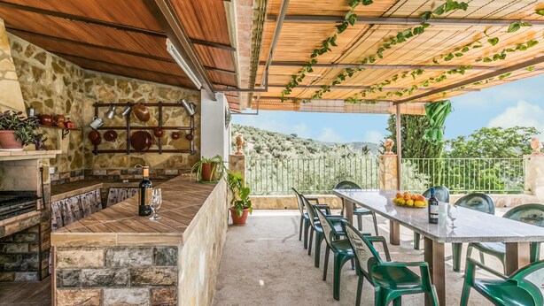 A covered outdoor dining area with stone walls, a wooden ceiling, and a view of the countryside.