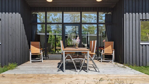 An outdoor seating area with a wooden table and chairs, large windows, and a view of trees. - 3 bedroom awesome home in Vig (Vig)