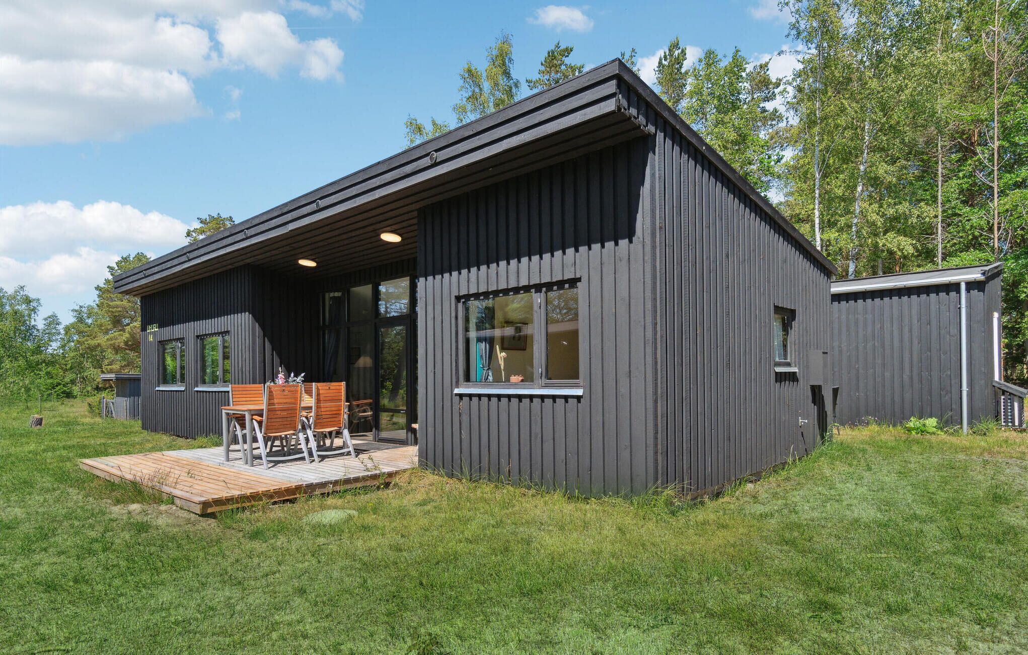 Eine moderne, dunkelholzgetäfelte Hütte mit einer Terrassenanlage, inklusive einem Holztisch und Stühlen.