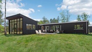 A modern black cabin with large windows, a patio with outdoor furniture, and a grassy yard. - 3 bedroom awesome home in Vig (Vig)