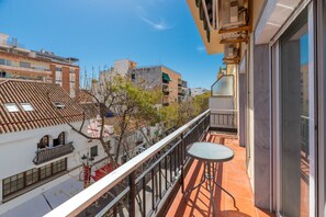 Un balcone con tavolo e sedie, vista su una strada con edifici e alberi.